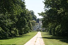 vue d'une allée bordée de chênes avec un le château des Genêts au fond