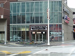 Exterior of the southern portion of Reserve Square, consisting of a three-story section including a lower level. The ground level entrance sign reads "WOIO-TV - WUAB-TV RAYCOM MEDIA STATIONS" with logos for "CBS 19", "19 ACTION NEWS" and "MY 43". A full size ad, "19 Action News: Honest, Fair, Everywhere" is at the corner of the building.