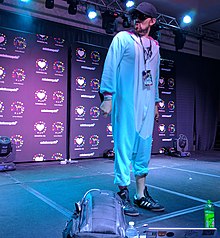 Photograph of a man in a Kigurumi with a microphone, vape, and Mountain Dew on the floor.