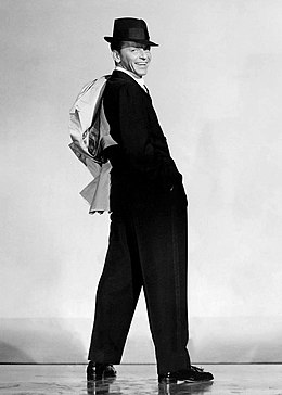 Photograph of Sinatra in a suit and hat looking over his shoulder to smile at the camera