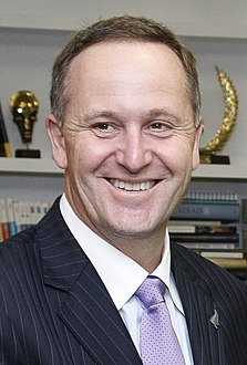 A man with brown eyes and short, brown hair wearing a white shirt, purple tie, and a black jacket with white pin-stripes.