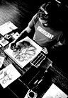 A black-and-white photo of a bearded man in an art studio