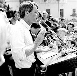 A black-and-white image of Kennedy speaking in a microphone