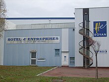 Photographie d'un bâtiment bas couvert de tôle ondulée peinte en bleu ciel et blanc avec des enseignes et un escalier de secours métallique marron en spirale