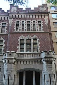 The First Battery Armory's western pavilion as seen from across 66th Street. The ground story contains a granite arch with a garage door, while the second and third stories contain a brick facade with granite-trimmed windows.