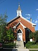A red brick church with windows that rise to pointed arches. The sky is blue with a few small clouds.
