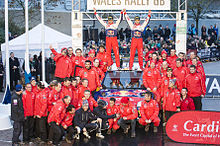 Sébastien Loeb et Daniel Elena debout sur le toit de leur Citroën C4 WRC, levant les bras au ciel et entourés de l'équipe de Citroën Racing.