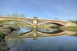 Two arches of a metal bridge separated by a stone pillar; the metalwork is painted red with cream details