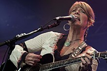 Country music singer Kathy Mattea singing into a microphone while strumming a guitar.