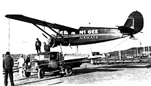 Black-and-white photo showing the left side of a seaplane being carried sideways on a truck
