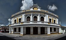 Color photo of a two-story building in white and yellow ochre, with neoclassical columns and ornamentation.