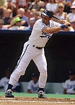 A photo of George Brett dressed in a white baseball uniform with a bat over his shoulders in home base