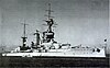 View of the Chilean battleship Almirante Latorre in the 1930s, under steam but apparently stationary in the water, a small steam launch lies close to her starboard side