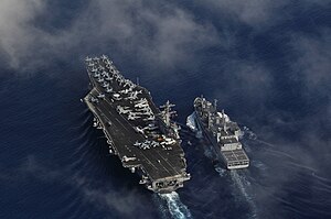 A supply ship refuels an aircraft carrier which has multiple aircraft on board