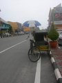 A trishaw parked by the roadside with Chukai town in the background.