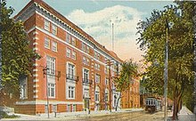 Exterior photo of a five-storey red brick building and street scene including a trolley car