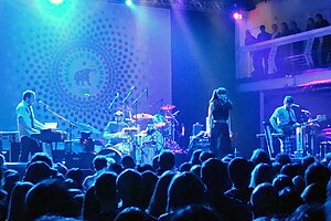 Four musician basking in turquoise and purple lights performing on stage in front of an audience