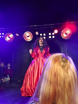 Drag queen in pink dress under red stage lighting