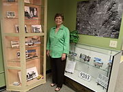 Dorothy Gunderson, of the Sunnyslope Historical Society and Museum, poses in front of the John C. Lincoln display in the historical building which once housed the "Peoples Drug Store".