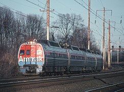 Stainless steel passenger railcars with horizontal red and blue stripes separated by thin white stripes. The visible end of the near car is red with a large blue stripe at the bottom, with "Amtrak" in large white letters.