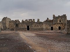 cour en terre battue, bâtiment en pierre entre deux tours