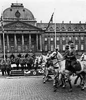 Photographie en noir et blanc montrant des cavaliers militaires défilant devant le palais.