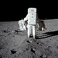 Photographie en couleur d'Aldrin en combinaison lunaire portant de boîtes d'expériences à mener sur la Lune.