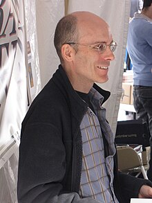 Photo of a bald, middle-aged man wearing glasses