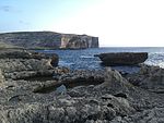 Bay with an islet and cliffs in the distance.