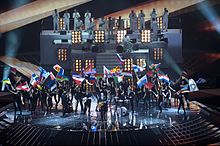 Photograph of the opening act during the 2011 contest; Stefan Raab performs with a band while multiple women dressed as Lena dance behind them while waving the flags of the participating countries