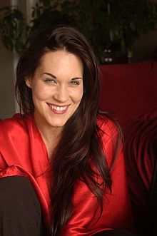 Teal Swan wearing a bright red top, grinning directly at camera