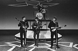 Monochrome image of The Beatles performing on a stage wearing dark suits