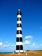 A black-and-white striped lighthouse, with the sea in the background