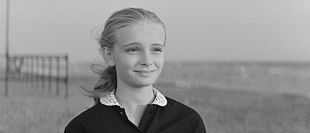 Visage d'une jeune fille blonde qui sourit avec la plage en arrière plan