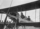 Photographie en noir et blanc de deux hommes assis en tandem dans les cockpits d'un biplan