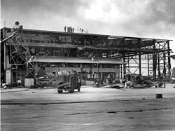 A large structure with most of the steel supports visible. Other materials that form the structure are burned, destroyed, and hanging off the steel. A fire truck sits parked in front.