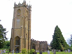 Stone building with arched windows and square tower. In the foreground are gravestones.