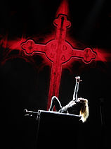 The silhouette of Madonna against a black backdrop featuring a red cross