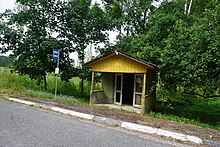 A little yellow bus stop amidst green trees