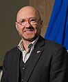 A bald white man with glasses. He is wearing a shirt and tie. There is a Scottish flag behind him.