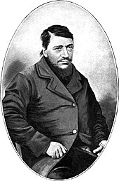 A man of about 40 with a large dark beard. The thumb on his left hand is absent.