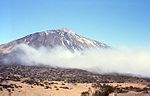 A ground view of a mountain top, obstructed by a few low-level clouds.