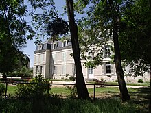 Photographie d'un bâtiment blanc vu à travers des arbres.