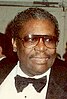 An elderly black man wearing suit and glasses