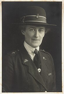 Portrait of a woman, bust, facing to her left with head turned to front, wearing military uniform and hat.