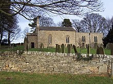 A stone wall in the foreground with graves and a small stone church beyond