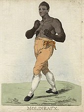 Hand-colored etching of a young shirtless black man in yellow pantaloons, high white socks, and black shoes. He stands on plain green ground before a plain white backdrop with both arms raised in front of him in a boxer's pose. His countenance appears innocent with eyebrows raised high. His left foot is stuck out in front of his right.