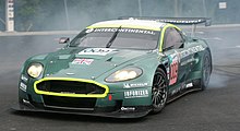 A dark green racing car, the DBR9, with much livery. It is shown drifting in action.