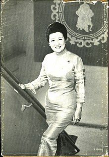 Black and white photograph of Chiang. She is standing on a flight of stairs, smiling and looking at the viewer, with her right hand on the banister located to the left. She is wearing a light-colored dress.