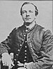 Head and torso of a white man with a tuft of hair on his chin, wearing a military jacket buttoned only at the neck.